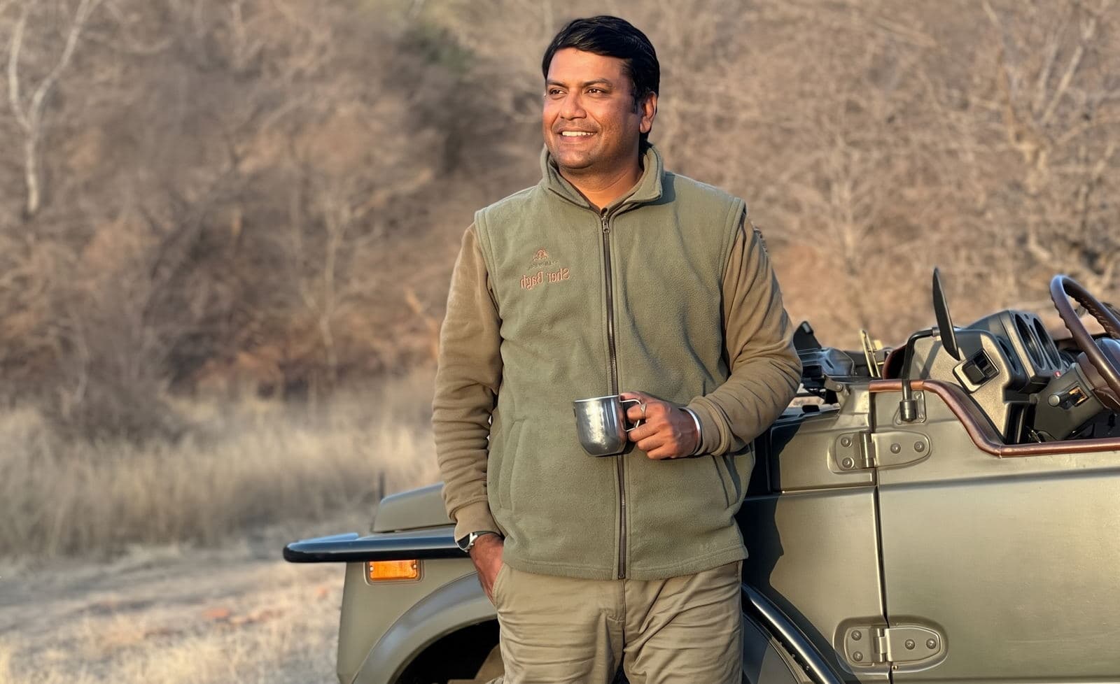 Vijay Kumawat standing beside an open safari vehicle in a dry Ranthambore forest landscape
